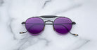 Front view of the Jacques Marie Mage Dasan titanium sunglass in black color with purple lenses on a white marbled with grey veining background