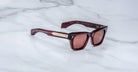 The Jacques Marie Mage Dealan 53 are rectangular dark red sunglasses with gold-accented arms, shown on a white marble surface.