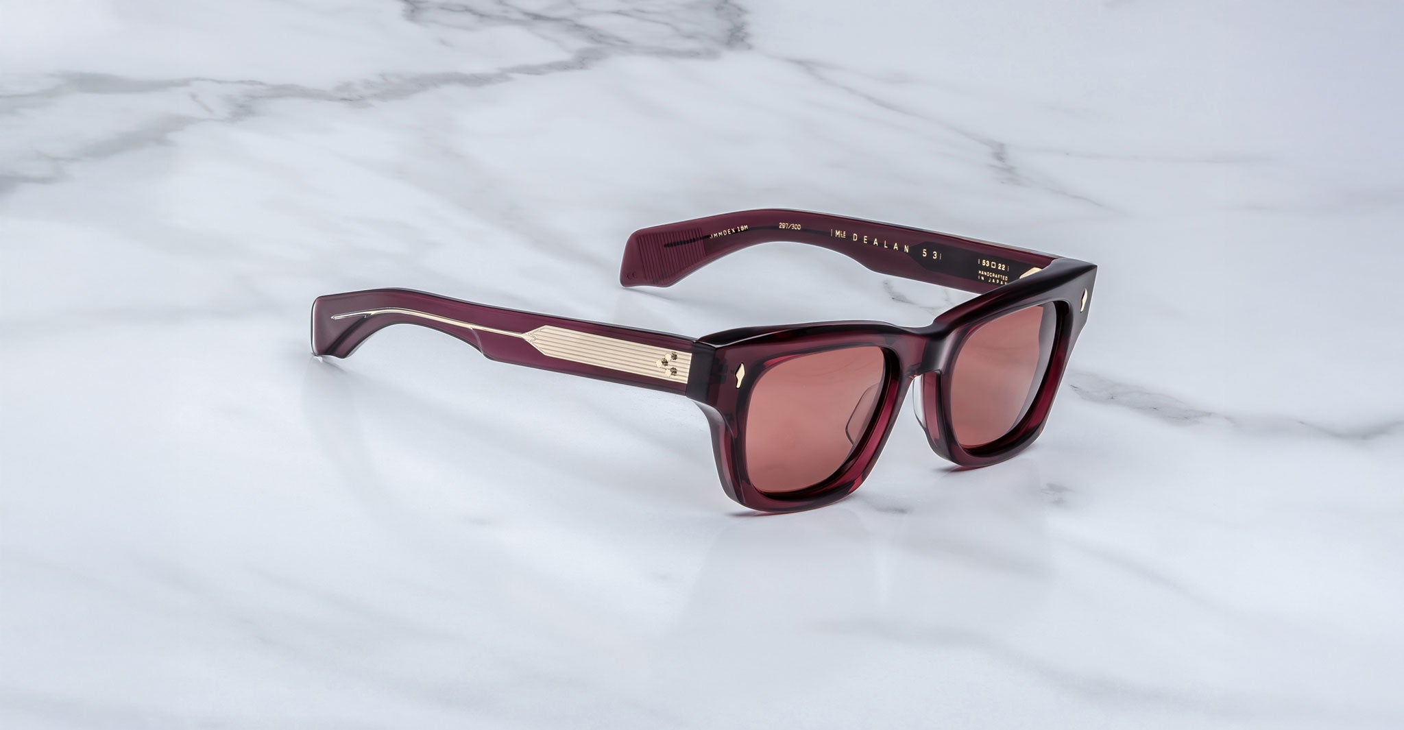 The Jacques Marie Mage Dealan 53 are rectangular dark red sunglasses with gold-accented arms, shown on a white marble surface.