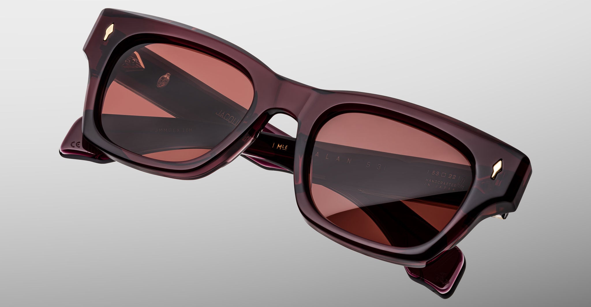 The Jacques Marie Mage Dealan 53 sunglasses, featuring square-shaped thick dark burgundy frames and reddish tinted lenses, are displayed against a light gray background.