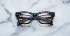 A pair of Jacques Marie Mage Dealan 53 tortoiseshell rectangular eyeglasses rests on a white marble surface, their lenses reflecting a multi-lane highway filled with vehicles and streetlights.