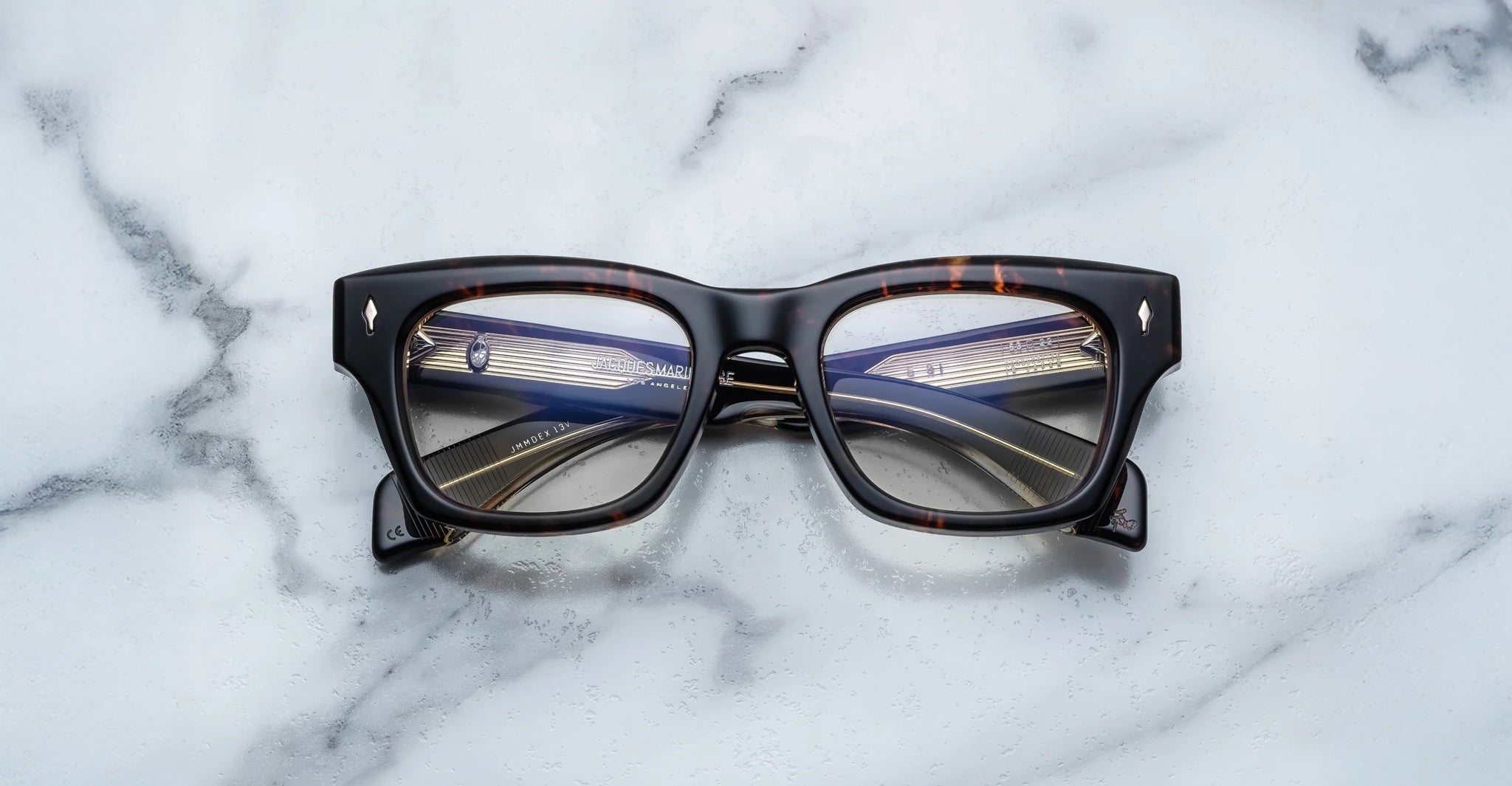 A pair of Jacques Marie Mage Dealan 53 tortoiseshell rectangular eyeglasses rests on a white marble surface, their lenses reflecting a multi-lane highway filled with vehicles and streetlights.