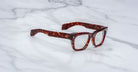 The Jacques Marie Mage Dealan 53 eyeglasses, featuring thick, rectangular tortoiseshell-patterned frames, are placed on a white marble surface.