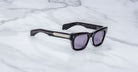 The Jacques Marie Mage Dealan 53 are black rectangular sunglasses with dark tinted lenses and wide temples, displayed on a light marble surface. Product information appears in white text inside the right temple.