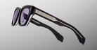 The Jacques Marie Mage Dealan 53 sunglasses, featuring black rectangular thick frames, tinted lenses, and silver metal temple detailing, are displayed against a gradient grey background to highlight the side and temple arms.