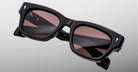 The Jacques Marie Mage Dealan 53 is a pair of black rectangular sunglasses with thick frames and dark tinted lenses, shown against a light gray background. Branding details and text appear on the inside of the arms.