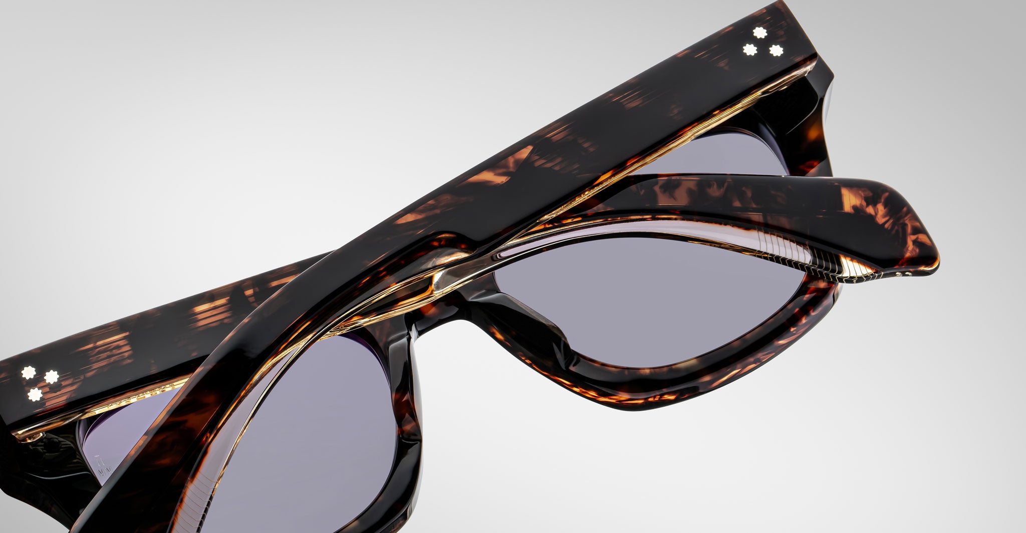 A close-up of Jacques Marie Mage Dealan tortoiseshell sunglasses with thick frames and dark lenses, viewed from above and behind the folded arms against a plain light background.