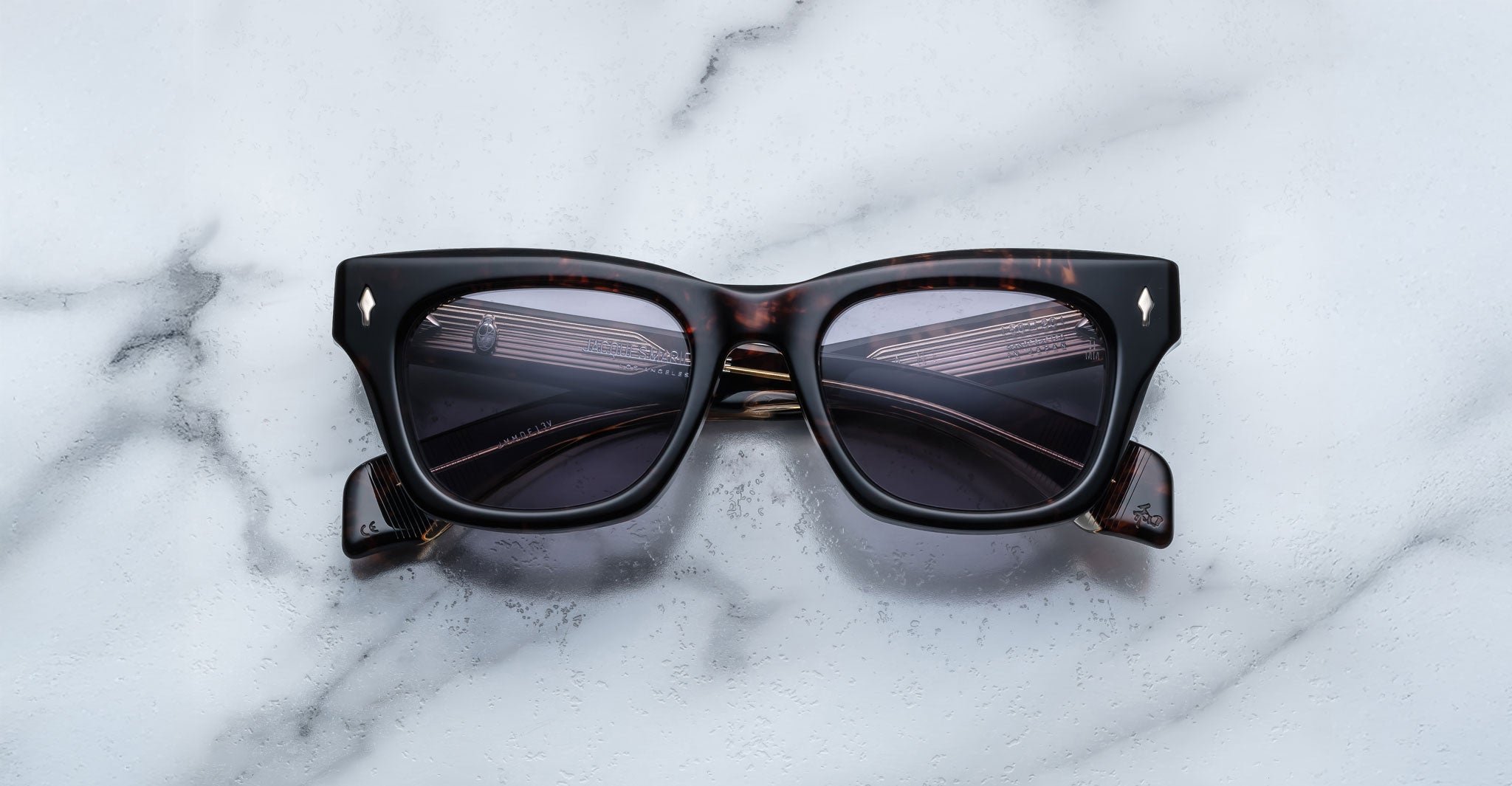 The Jacques Marie Mage Dealan rectangular sunglasses in dark tortoiseshell with dark lenses are displayed on a white marble surface.