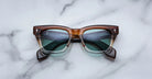 Jacques Marie Mage Dealan square eyeglasses with green lenses are shown from above on a flat surface.