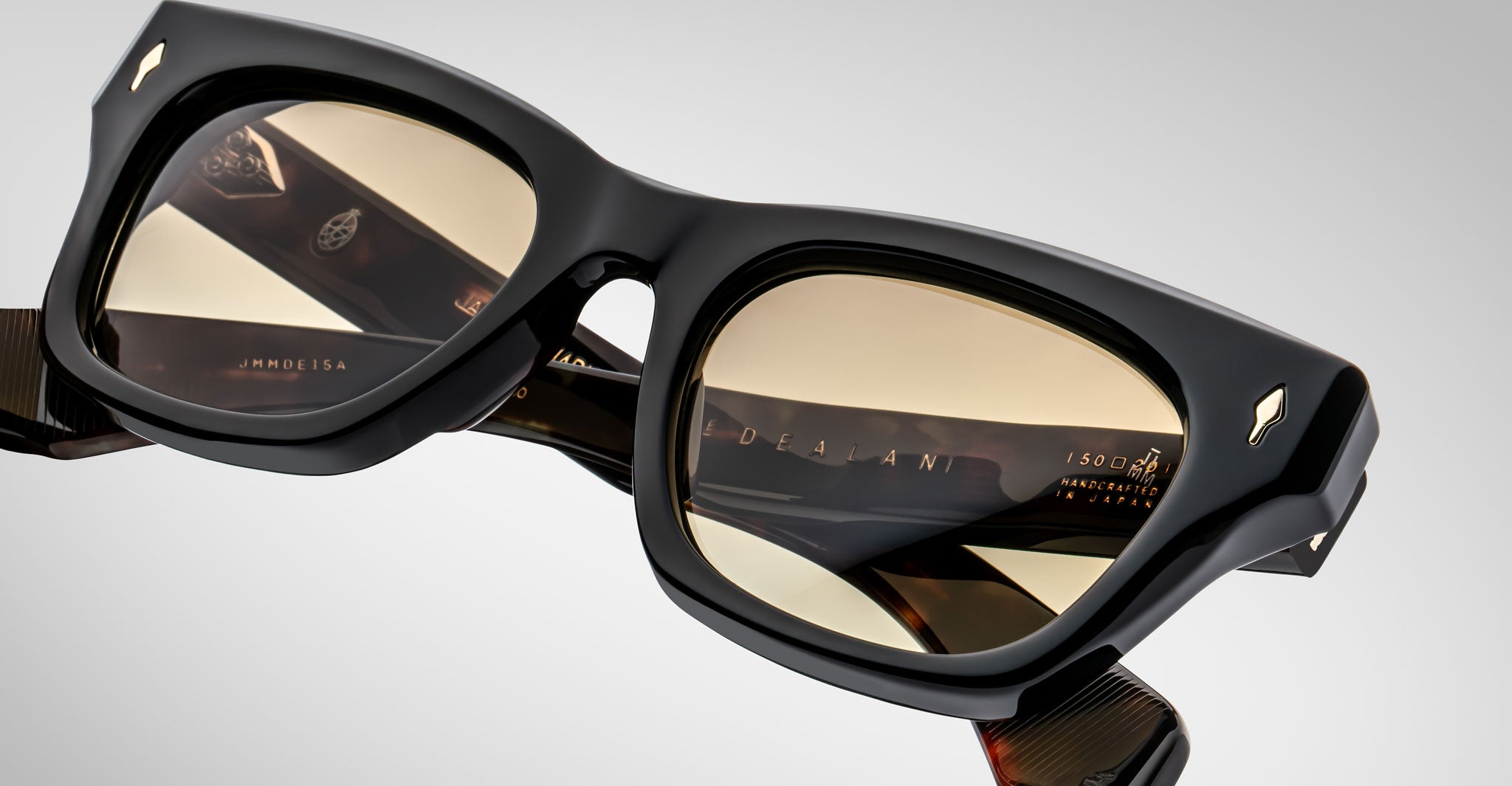 Close-up of Jacques Marie Mage Dealan black rectangular eyeglasses with thick frames and light brown tinted lenses, featuring reflected highlights and inner markings on the arms against a neutral background.