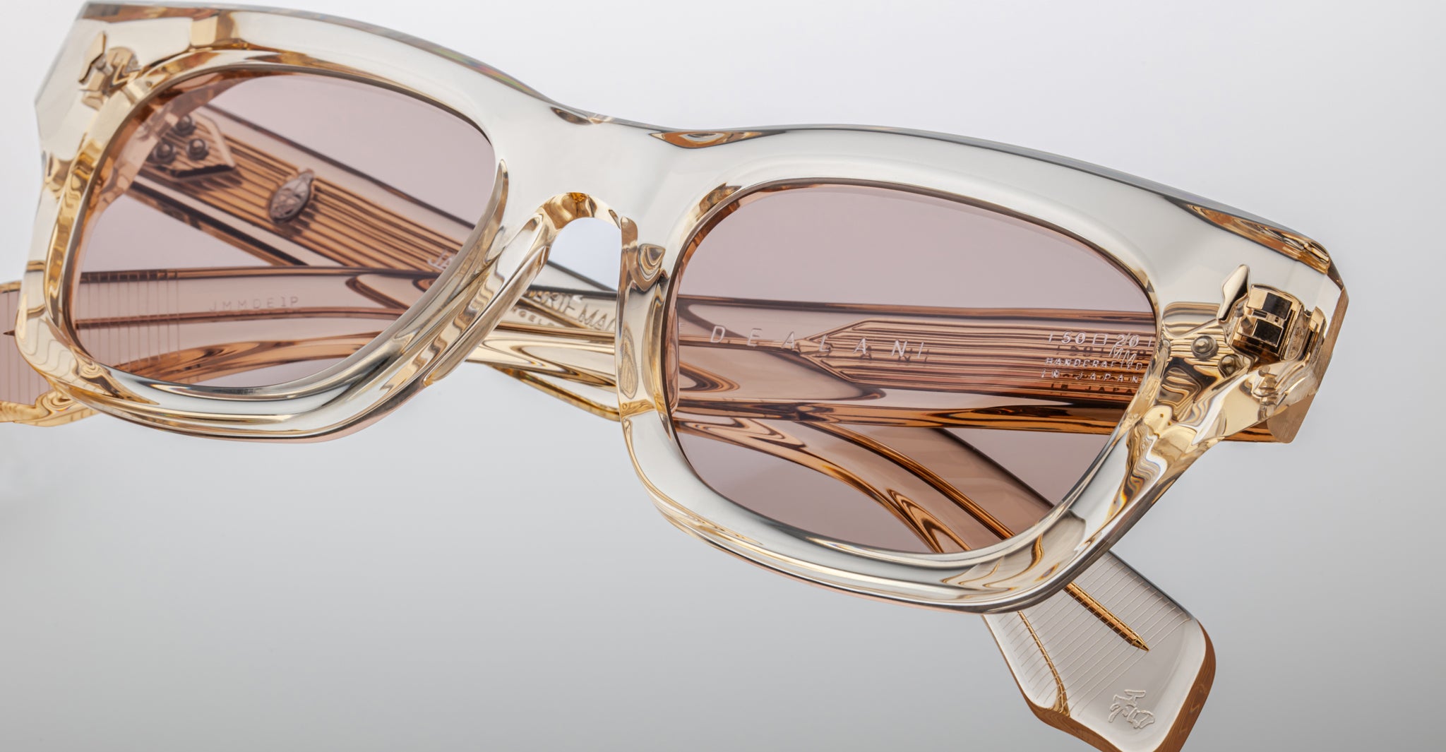 Close-up of Jacques Marie Mage Dealan sunglasses featuring light tan translucent rectangular frames and brown tinted lenses, set against a light background to highlight frame details and reflections.