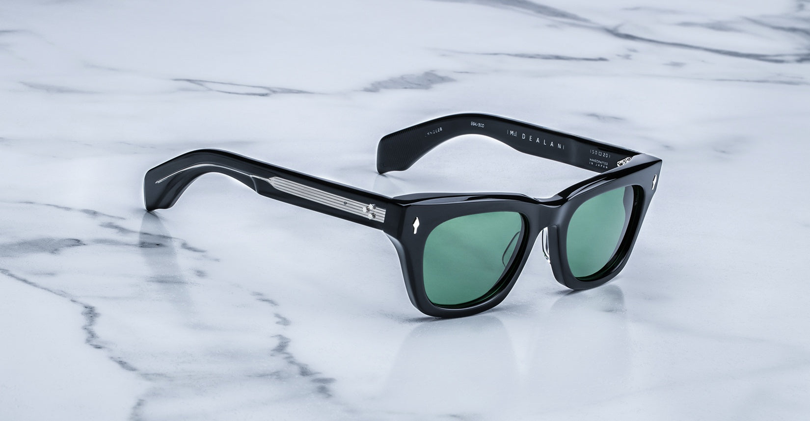 Jacques Marie Mage Dealan sunglasses with green lenses and metal accents, viewed from above.