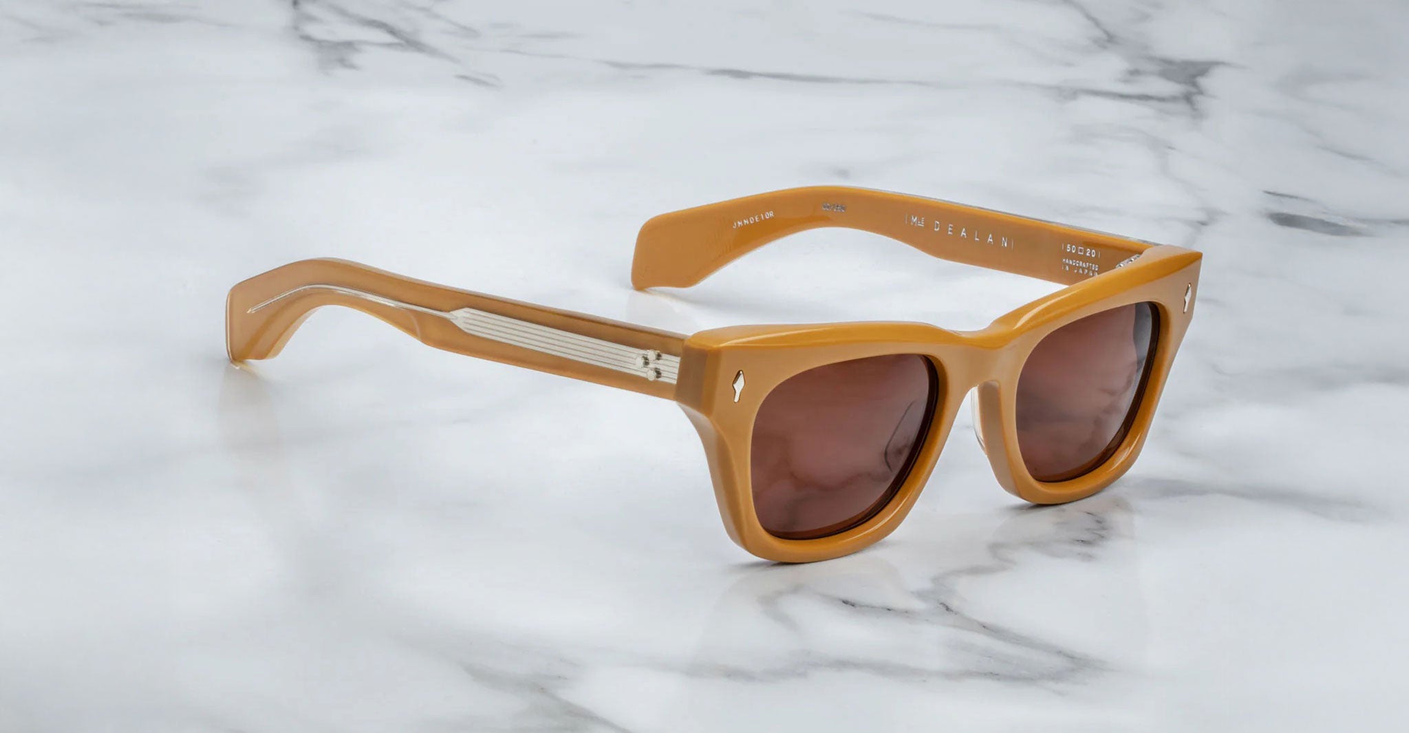 Profile view of Jacques Marie Mage Dealan acetate sunglasses in a tan color with dark lenses, sitting on a marbled background