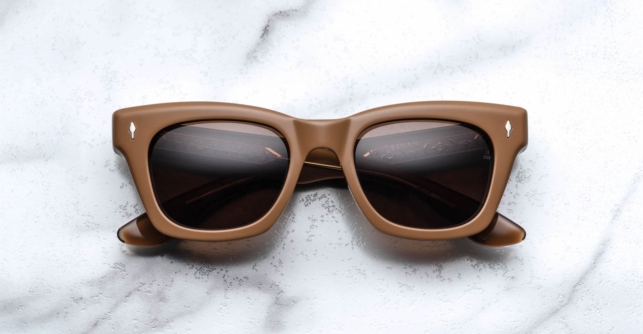 The Jacques Marie Mage Dealan X Umit Benan brown square-framed sunglasses with dark lenses are displayed on a white marble surface.