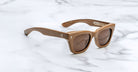 The Jacques Marie Mage Dealan X Umit Benan are brown rectangular sunglasses with thick frames and dark lenses, shown on a white marble surface. The temples have small decorative details near the hinges.