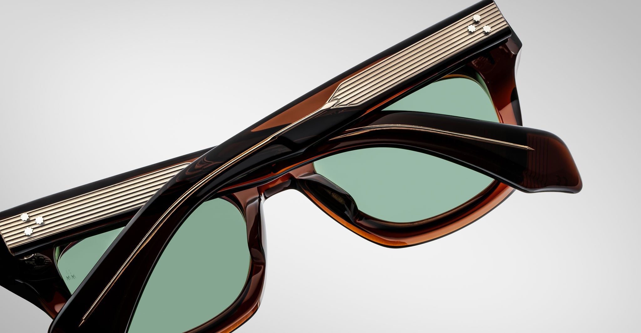 Close-up of Jacques Marie Mage Dealan sunglasses with green-tinted lenses, tortoiseshell brown frames, and gold accents detailed with horizontal lines along the top edge.