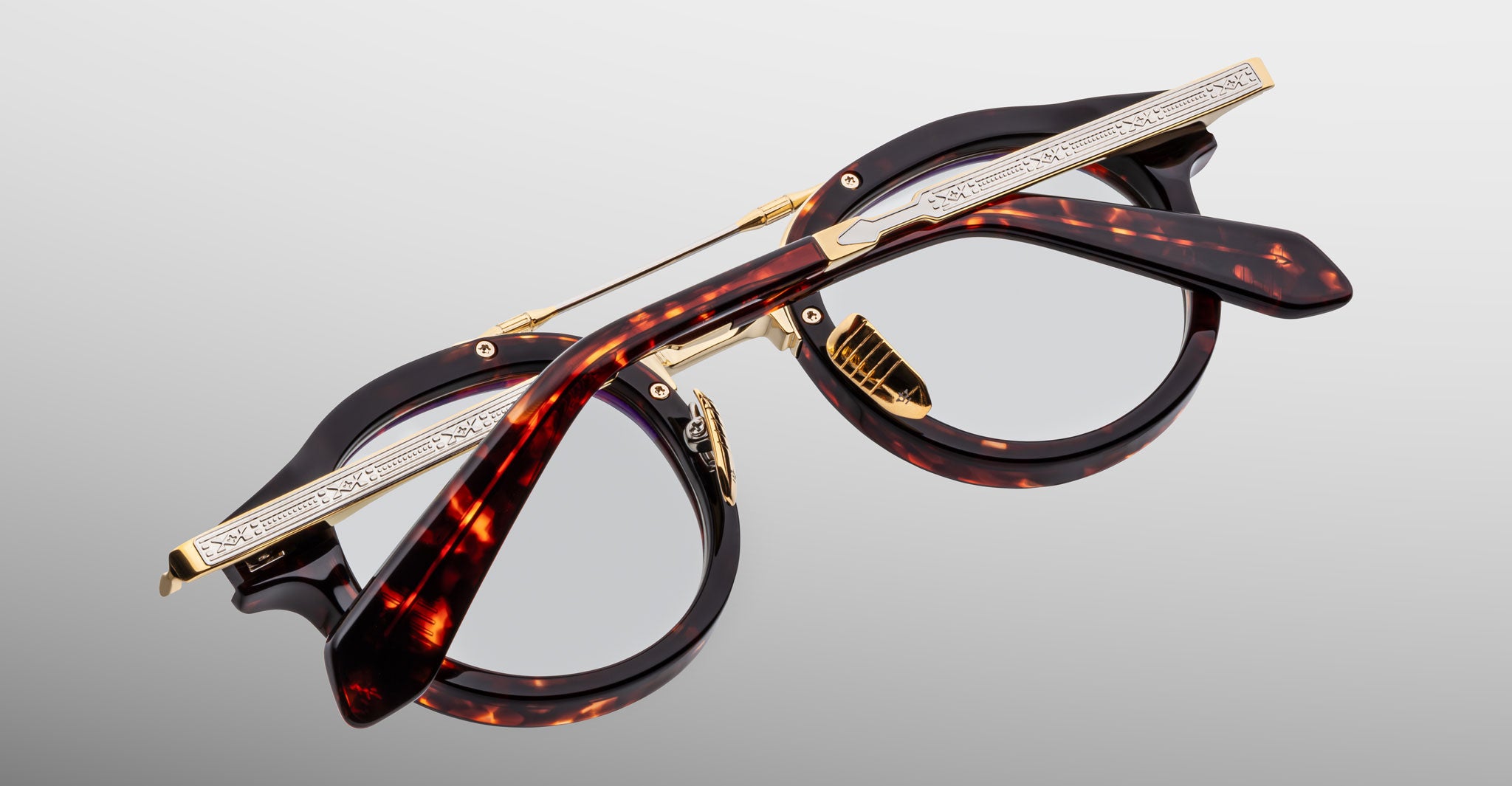 The Jacques Marie Mage Delage round eyeglasses feature tortoiseshell frames and gold metal accents, pictured partially folded on a plain light gray background.