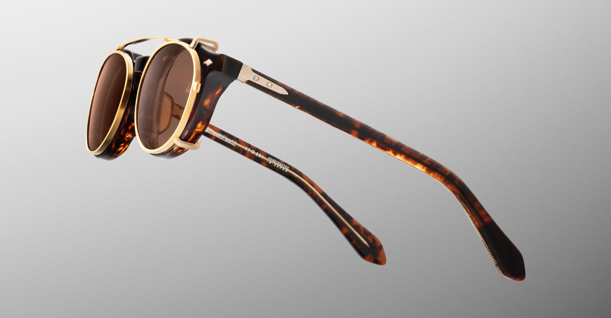 Jacques Marie Mage Demoncey Clip-On sunglasses, round brown lenses, gold accents, top-down view.