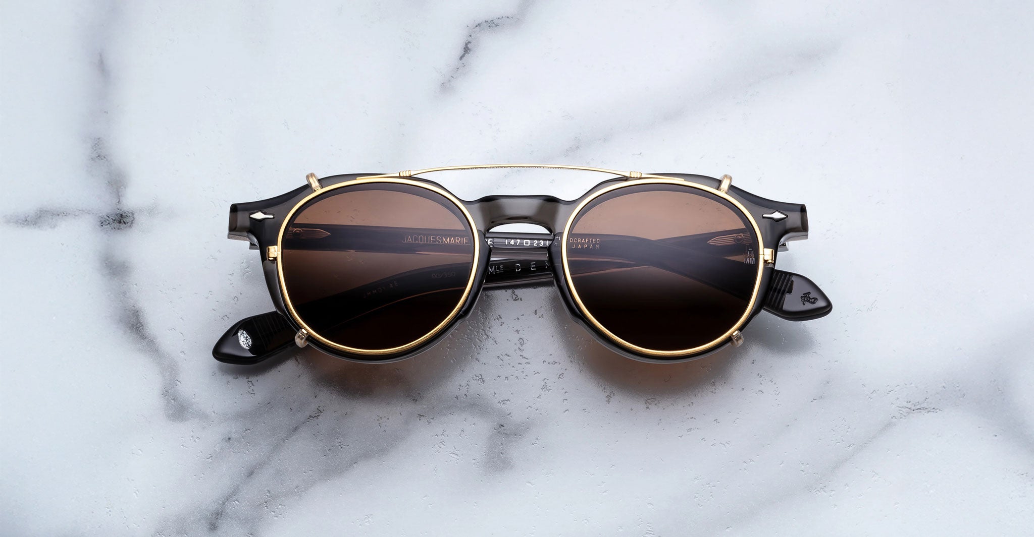 Jacques Marie Mage Demoncey Clip-On sunglasses with gold frames and dark lenses, top view.