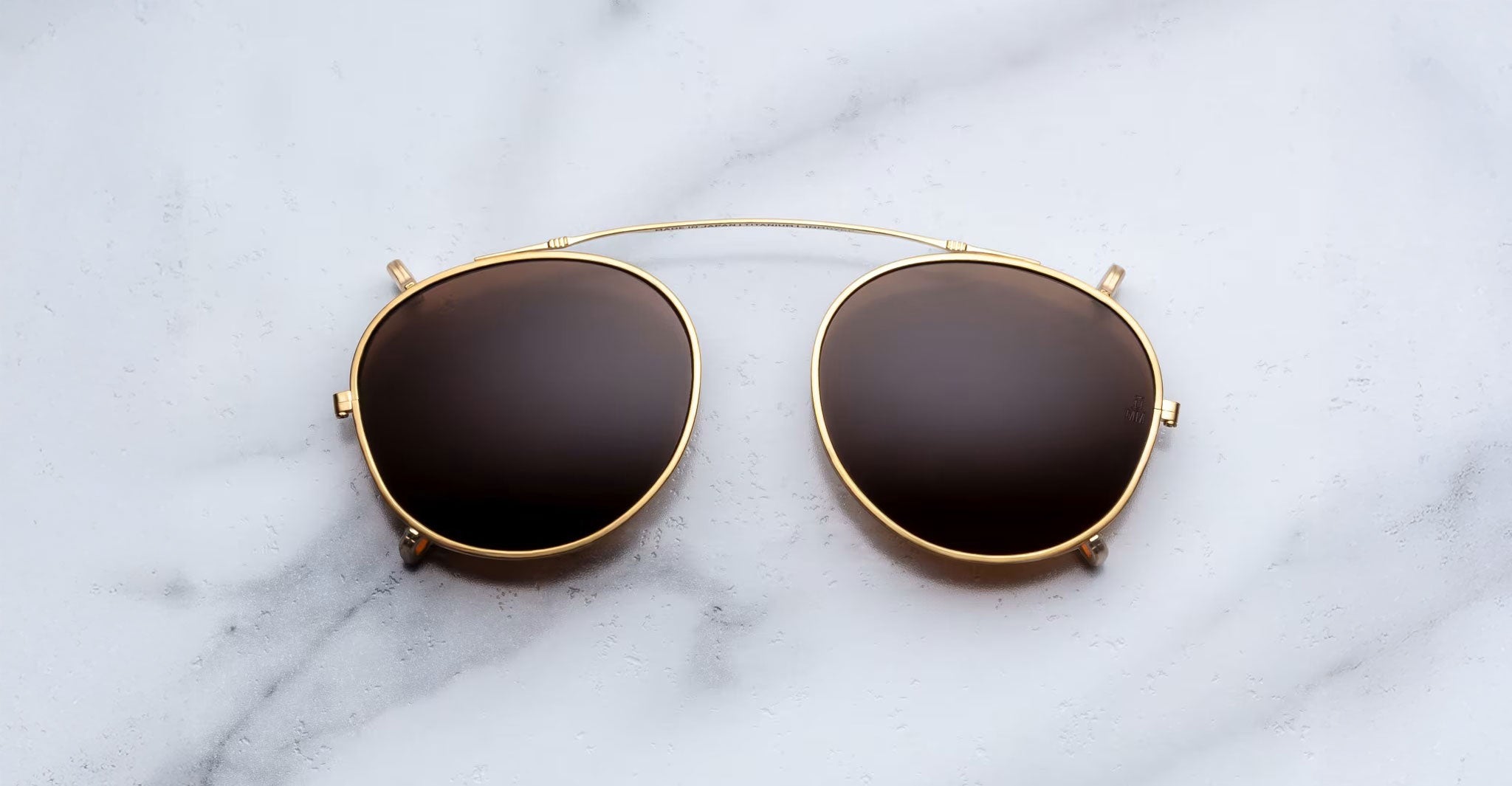 Jacques Marie Mage Demoncey Clip-On sunglasses with dark lenses and gold frames, top view.