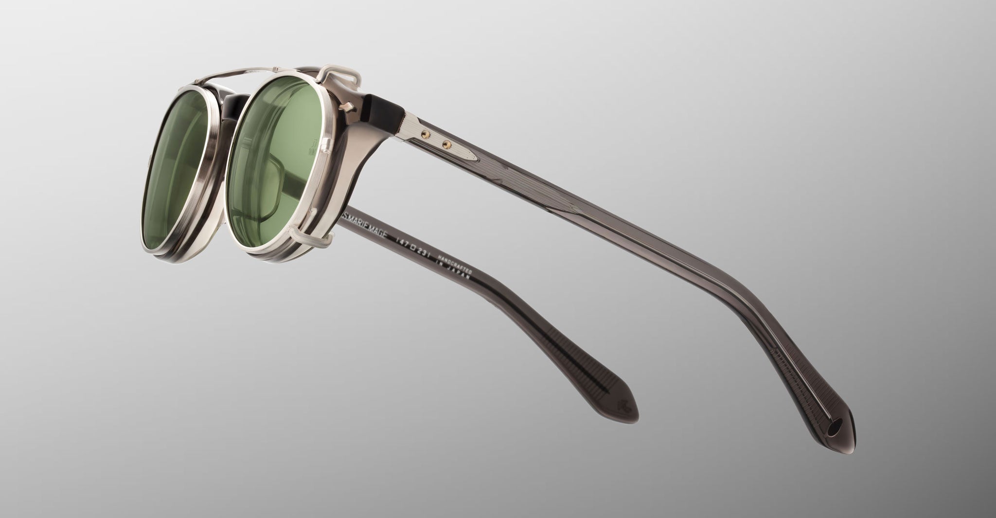 Jacques Marie Mage Demoncey Clip-On eyeglasses feature round green lenses, silver frames, and sturdy arms, shown from a side angle.