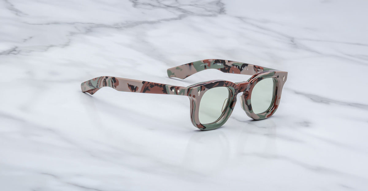 3/4 view of Jacques Marie Mage Devaux optical frame in Sergeant camoflauge pattern with clear lenses on a marbled background