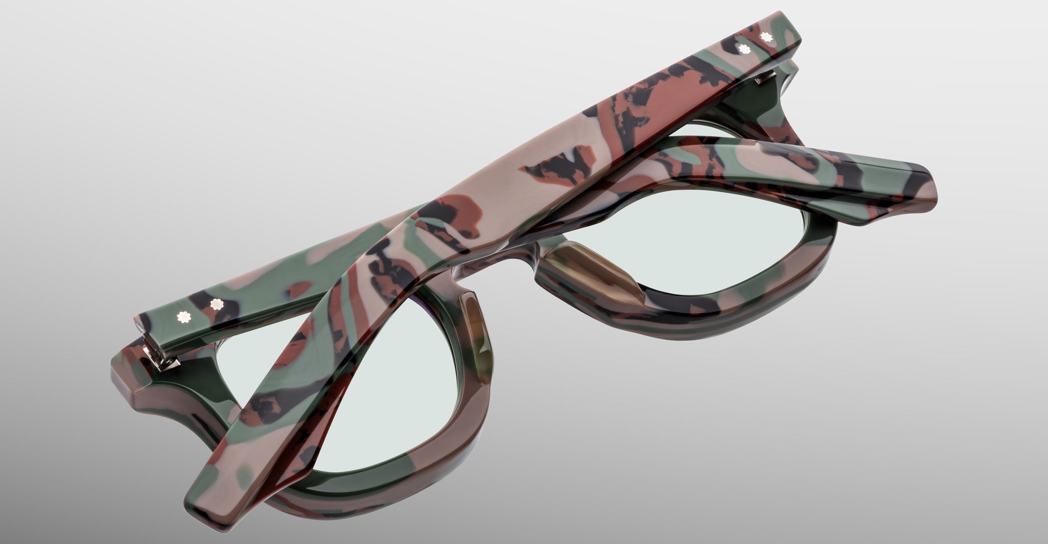 Back view of Jacques Marie Mage Devaux optical frame in Sergeant camoflauge pattern with clear lenses and folded temples on a light gray background