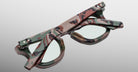 Back view of Jacques Marie Mage Devaux optical frame in Sergeant camoflauge pattern with clear lenses and folded temples on a light gray background