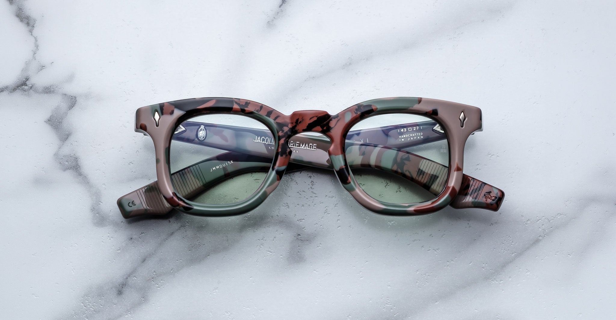 Front view of Jacques Marie Mage Devaux optical frame in Sergeant camoflauge pattern with clear lenses and folded temples on a marbled background