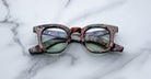 Front view of Jacques Marie Mage Devaux optical frame in Sergeant camoflauge pattern with clear lenses and folded temples on a marbled background