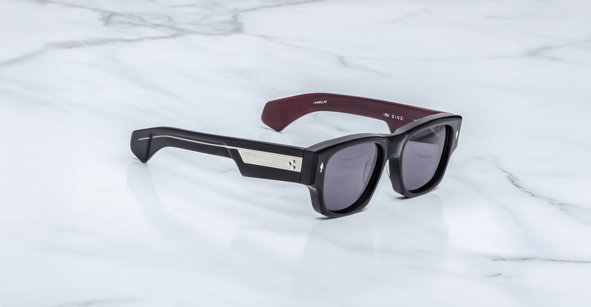 Jacques Marie Mage Dino in Bloodstone black acetate sunglass frame with grey lenses, gold arrowhead pins, and sculptural wide temples, three-quarter view showing front and temple profile