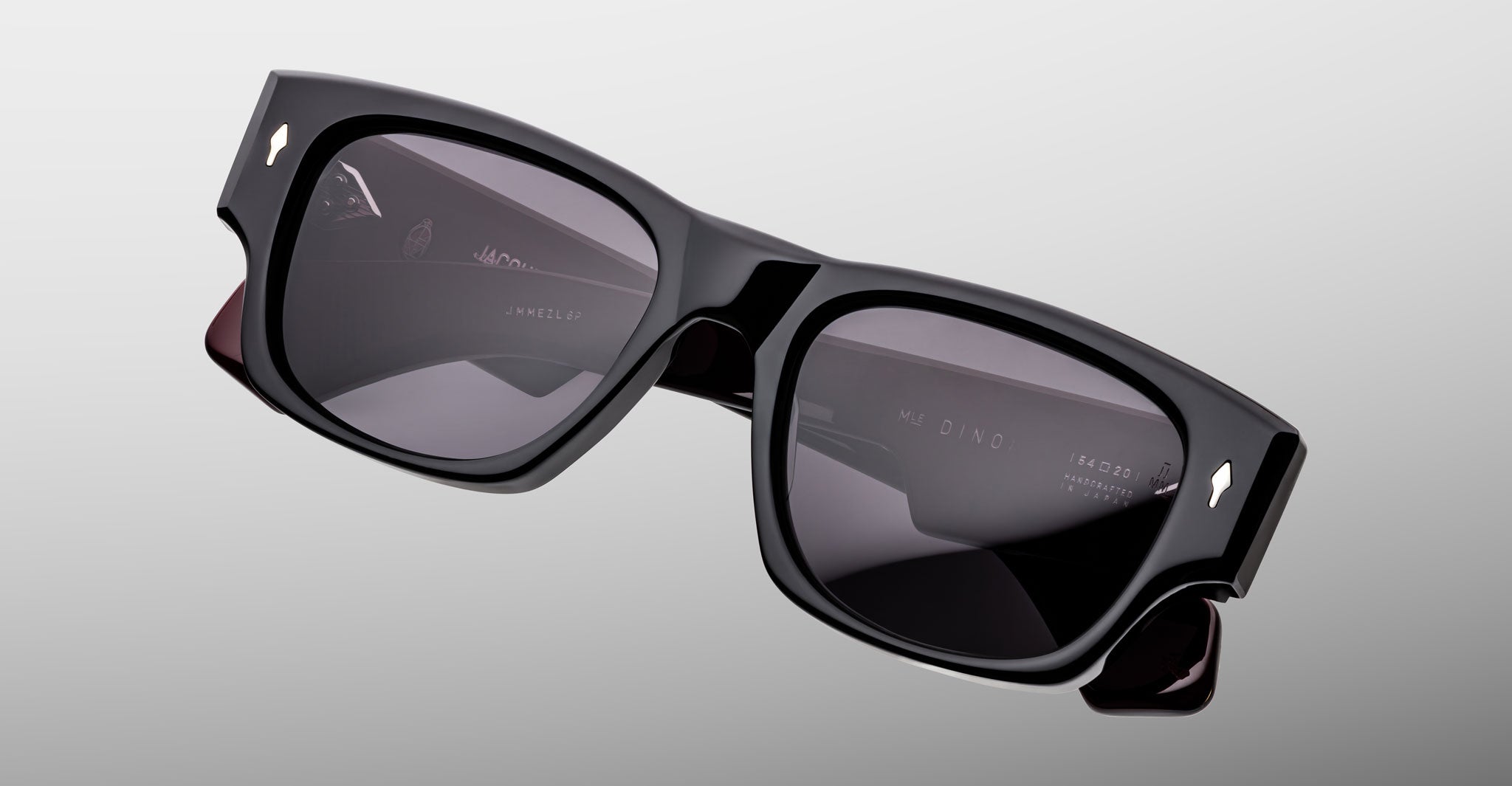 Jacques Marie Mage Dino in Bloodstone black acetate sunglass frame with grey lenses, gold arrowhead pins, and sculptural wide temples, angled top view showing lens and bridge detail
