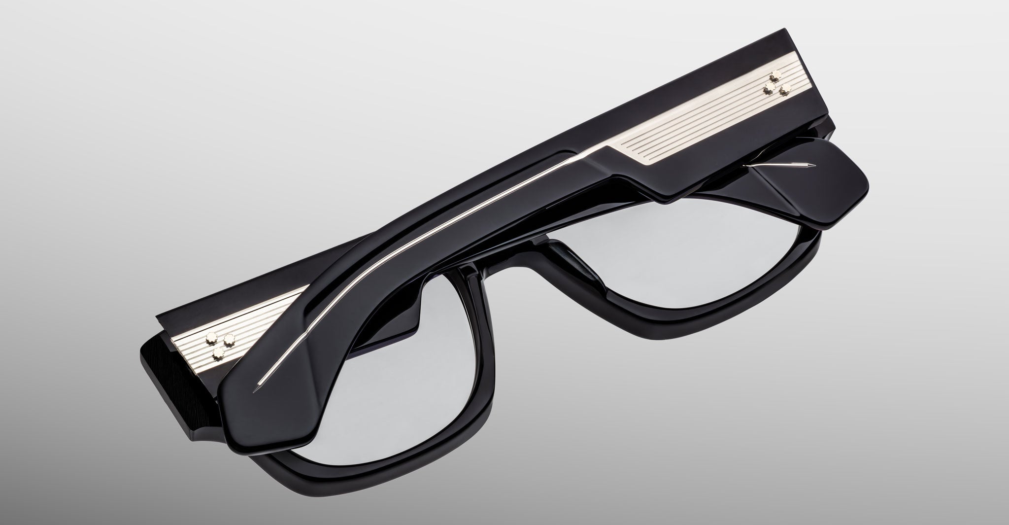 Jacques Marie Mage Dino in Bloodstone black acetate optical frame with clear lenses, gold arrowhead pins, and sculptural wide temples, angled view highlighting layered temple construction and wirecore detail