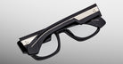 Jacques Marie Mage Dino in Bloodstone black acetate optical frame with clear lenses, gold arrowhead pins, and sculptural wide temples, angled view highlighting layered temple construction and wirecore detail