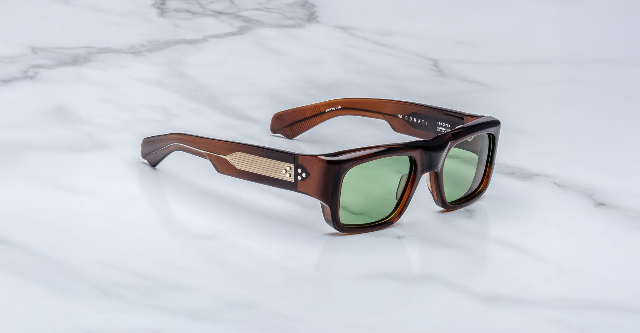 Jacques Marie Mage Donat rectangular sunglasses with thick brown tortoiseshell frames, green lenses, and metallic temple accents, shown on a white marble surface.