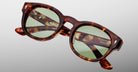 Close-up of Jacques Marie Mage Dr. Dream sunglasses in a tortoiseshell frame with green tinted lenses, displayed on a plain light gray background.