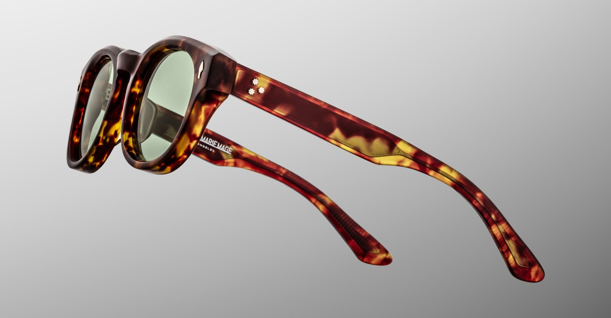 The Jacques Marie Mage Dr. Dream sunglasses by Jacques Marie Mage feature a round, tortoiseshell pattern and green tinted lenses inspired by handcrafted Japanese glasses, shown against a plain grey background.