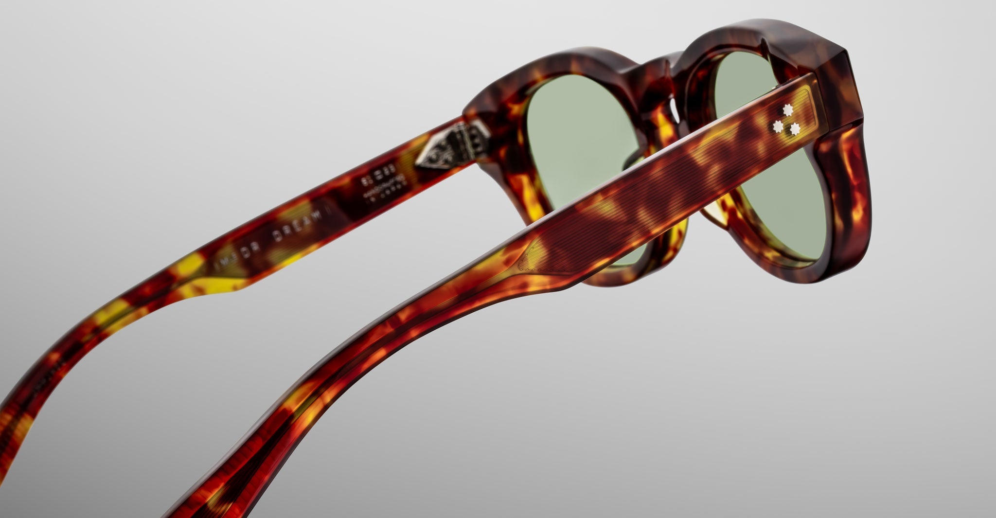 Close-up of Jacques Marie Mage Dr. Dream sunglasses, showcasing luxury tortoiseshell frames with green lenses, viewed from the side and back against a plain light background.
