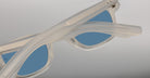 Close-up of Jacques Marie Mage Zephirin sunglasses in translucent white with blue lenses, shown angled with crossed arms—a stunning, limited edition model from Jacques Marie Mage.