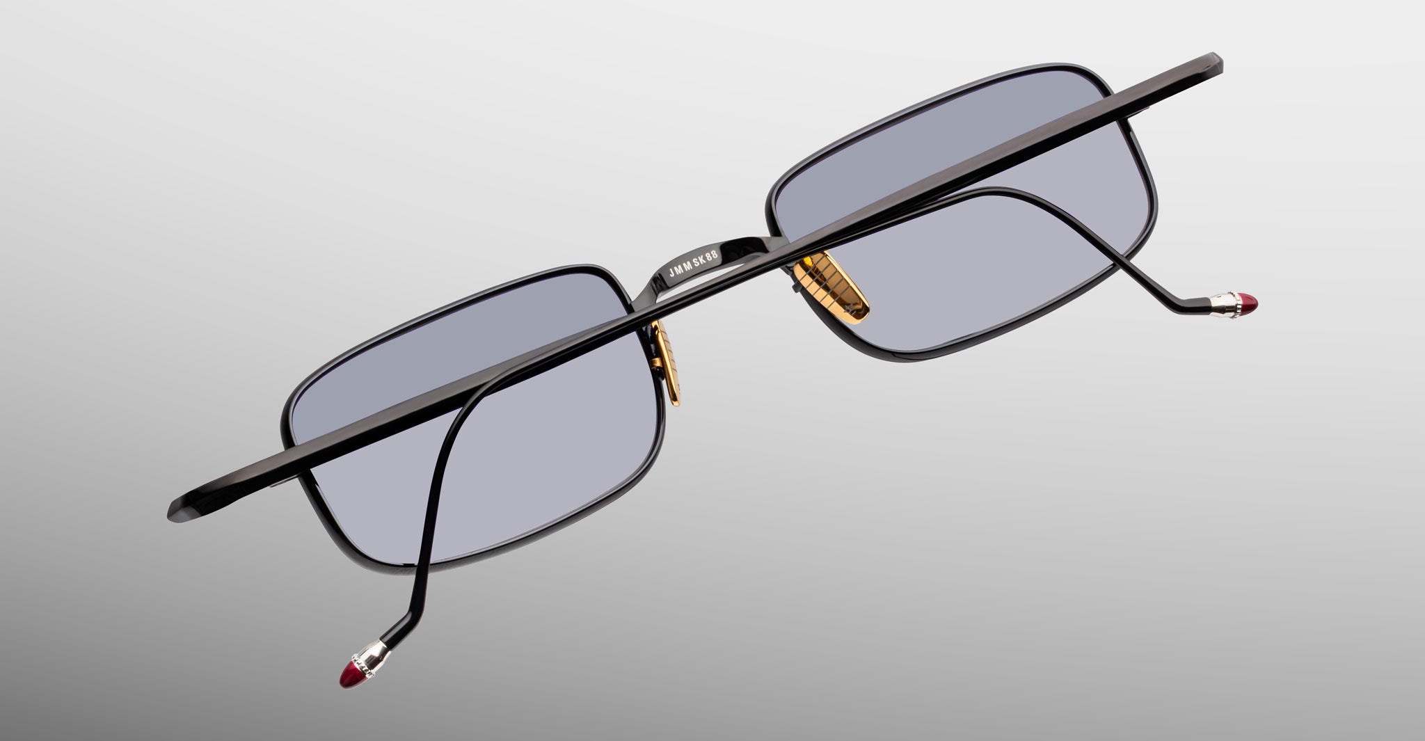 Jacques Marie Mage Dusk sunglasses with black frame, gold nose pads, and red arm tips shown from side angle.