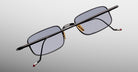 Jacques Marie Mage Dusk sunglasses with black frame, gold nose pads, and red arm tips shown from side angle.
