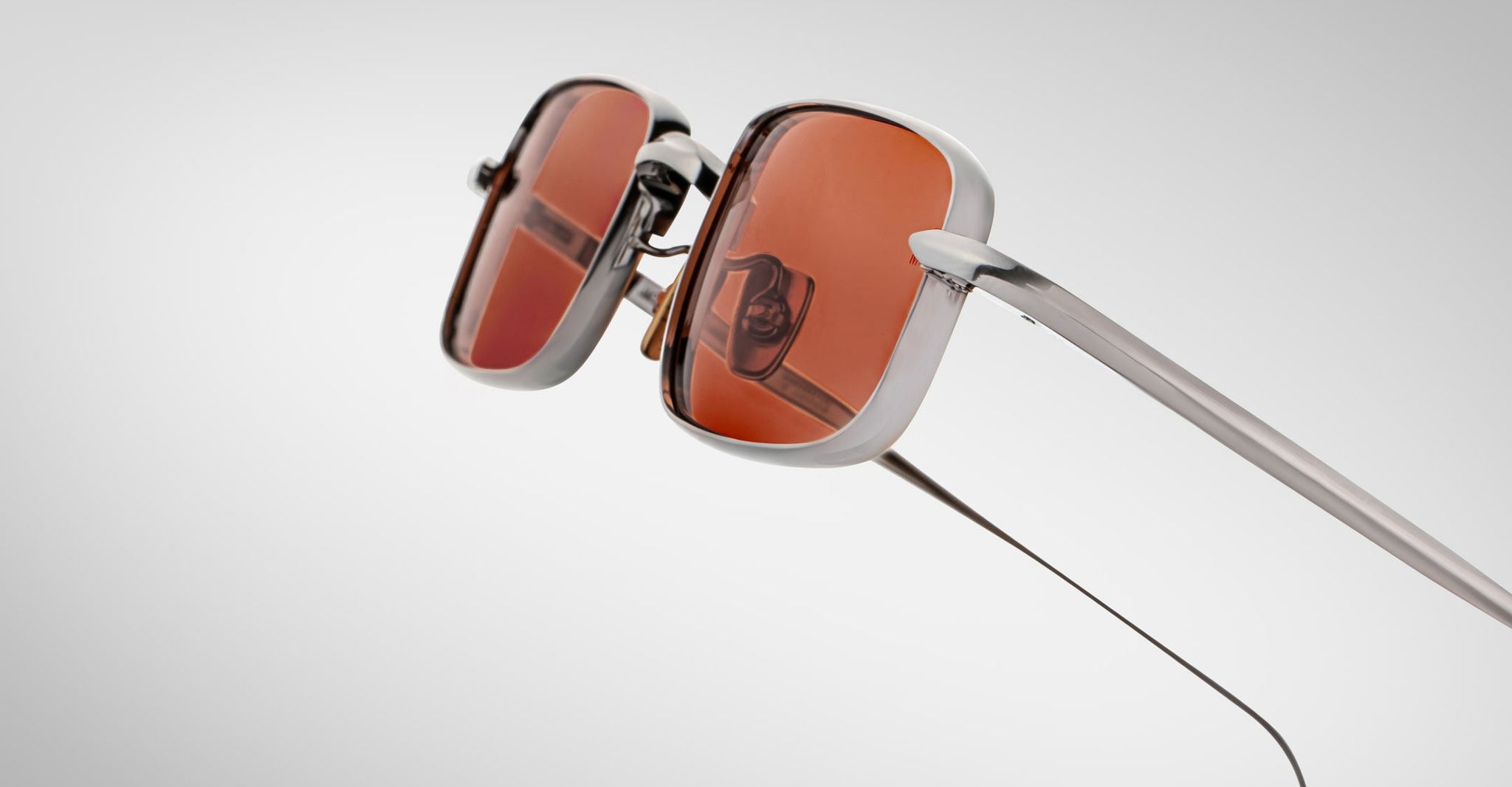 Close-up view of Jacques Marie Mage Dusk sunglasses featuring metallic silver frames and red-tinted lenses, set against a plain light gray background.