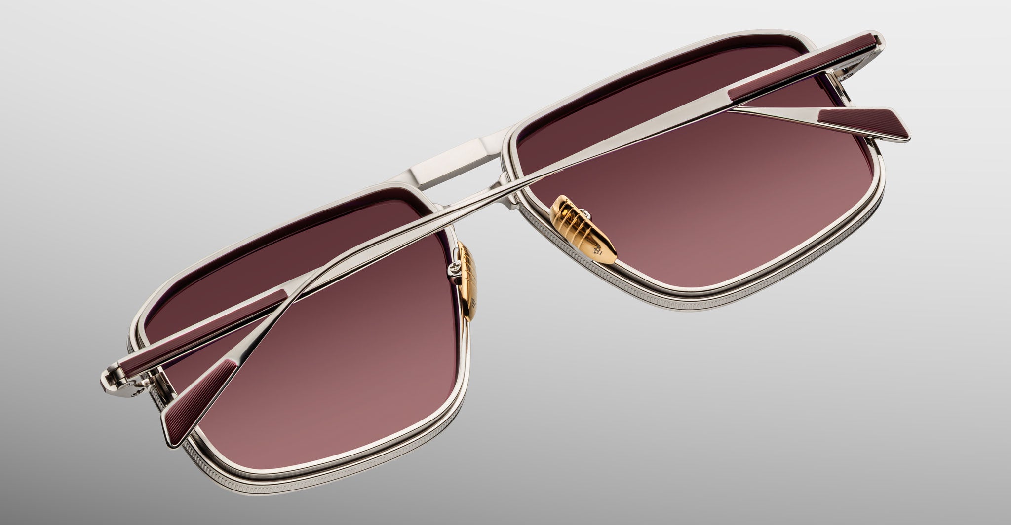 Close-up of Jacques Marie Mage Earl sunglasses showing pink-tinted lenses and angular temples, viewed from the side.