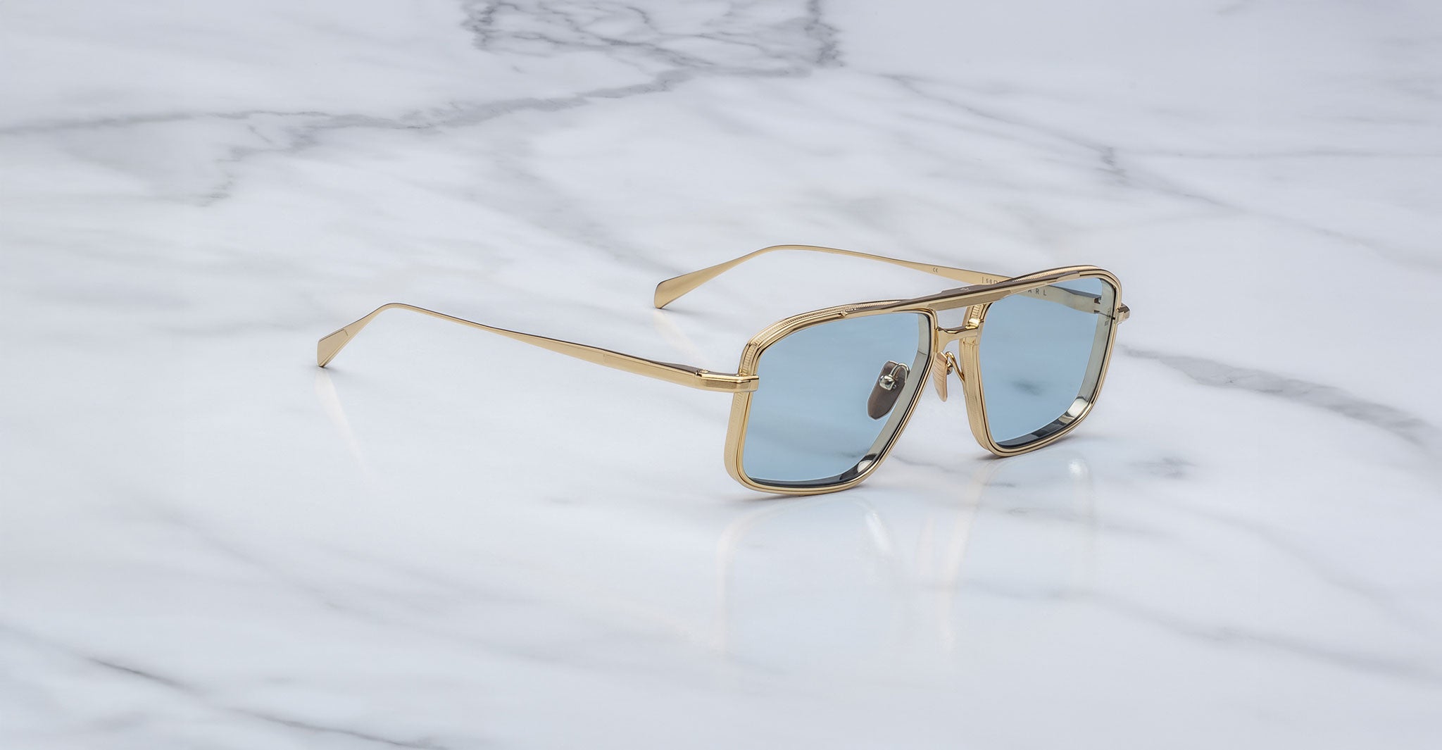 Jacques Marie Mage Earl sunglasses with gold frames and blue-tinted lenses, top view.