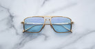 Jacques Marie Mage Earl sunglasses with gold frames and blue lenses, shown from above.