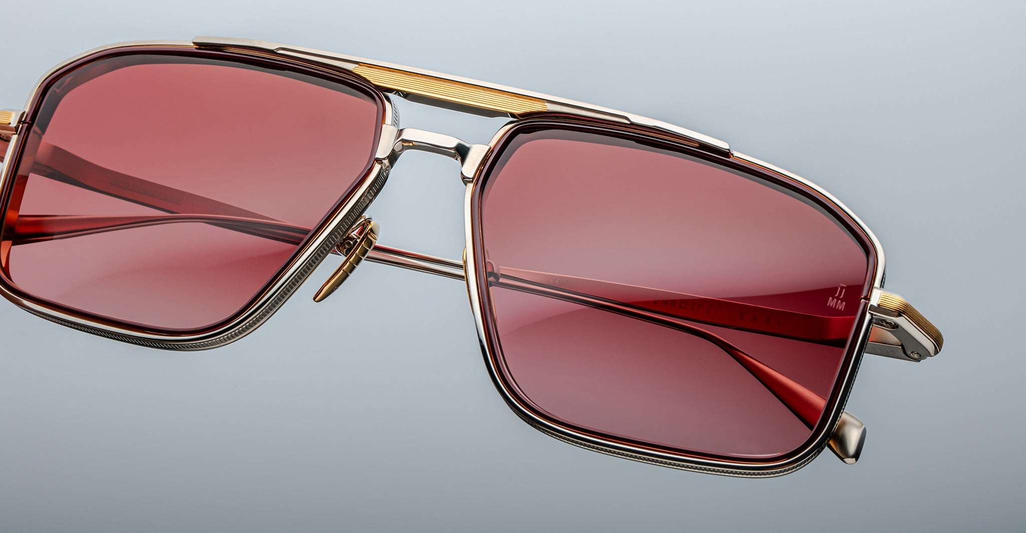 Close-up of Jacques Marie Mage Earl gold-framed sunglasses with red rectangular lenses, front view.