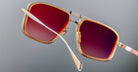 Angled side view of Jacques Marie Mage Earl sunglasses in retro gold frame with red-tinted lenses.