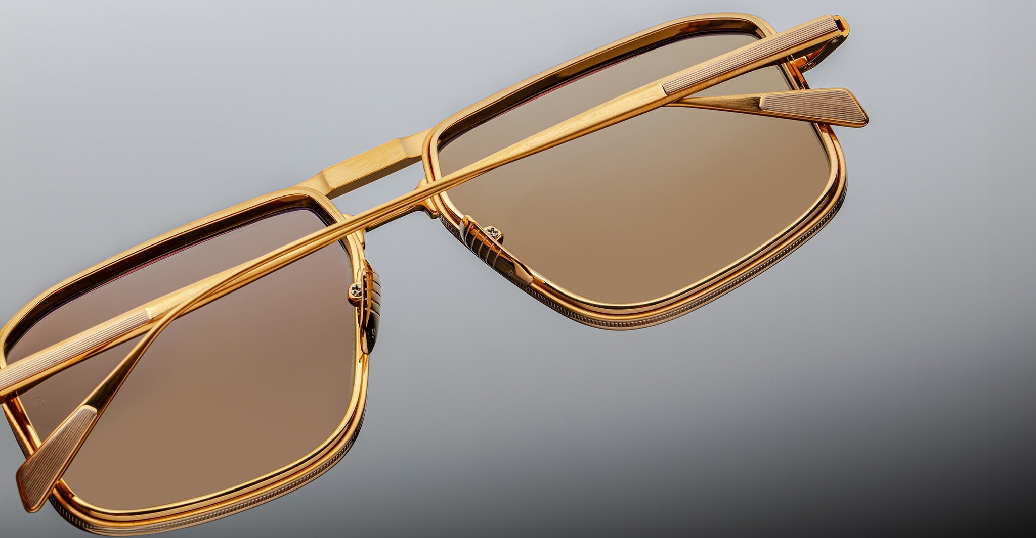 Close-up of Jacques Marie Mage Earl gold rectangular sunglasses with brown polarized lenses, viewed from above.