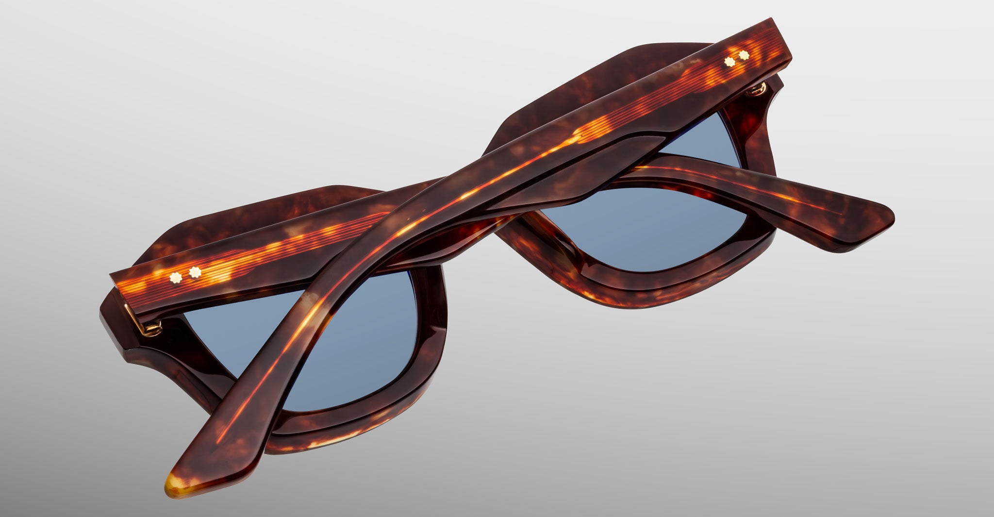 The Jacques Marie Mage Eichler sunglasses feature a tortoiseshell frame with blue lenses, displayed folded and viewed from the back on a light gray background.