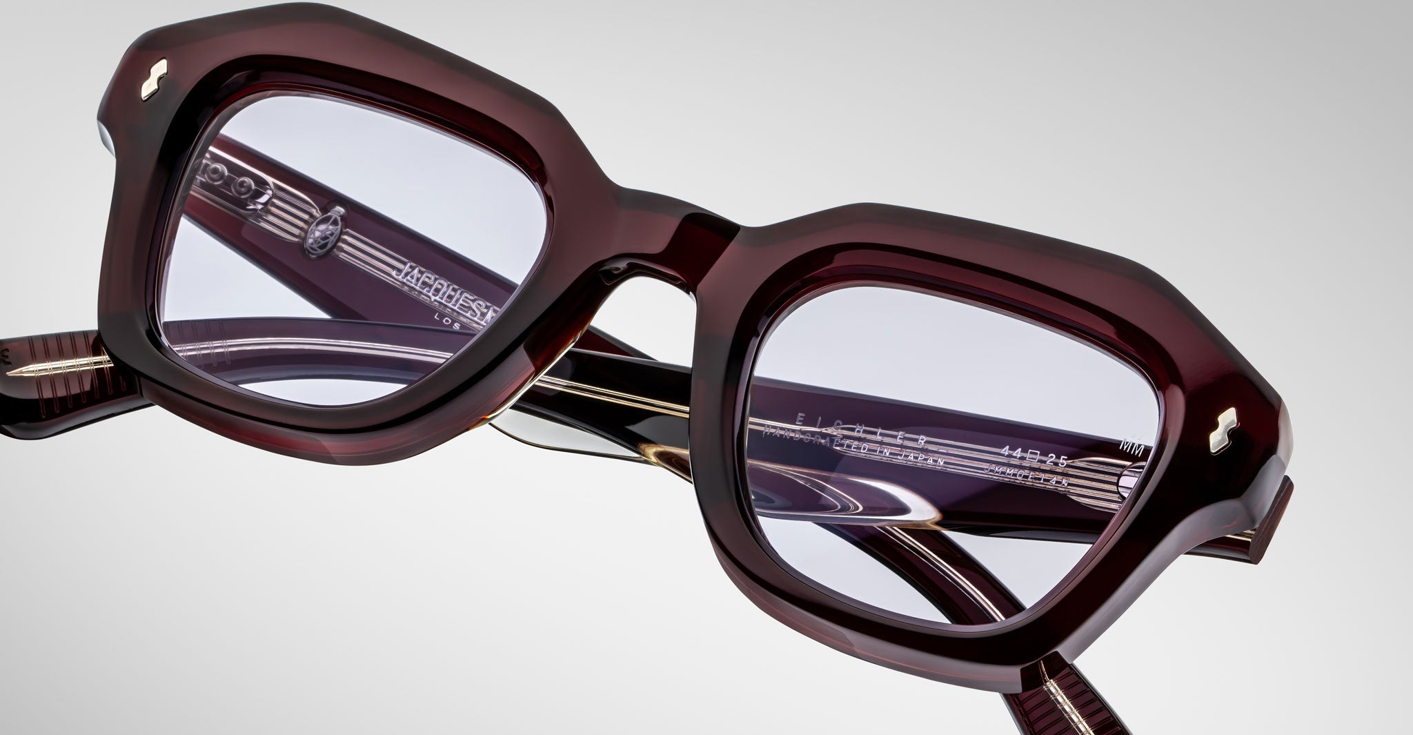Detailed front view of a pair of Jacques Marie Mage Eichler cherry, thick-framed sunglasses with lilac lenses on a plain background